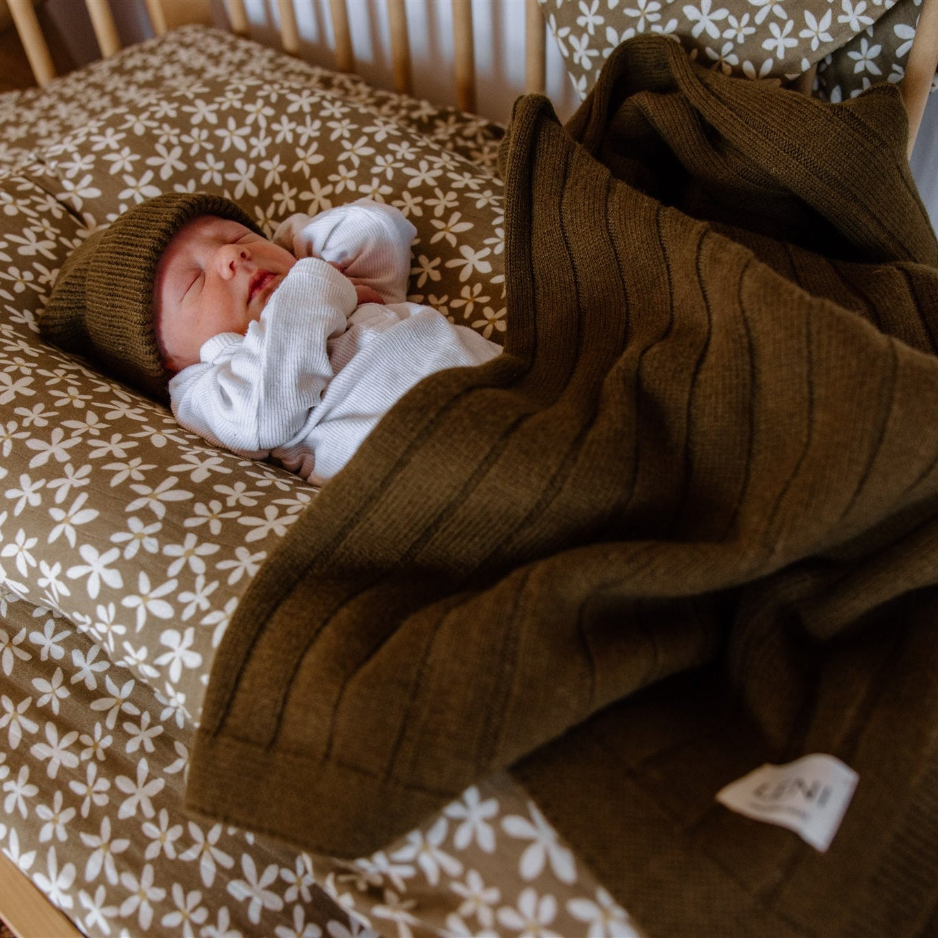 Newborn baby in a crib with a Olive green blanket and knitted hat