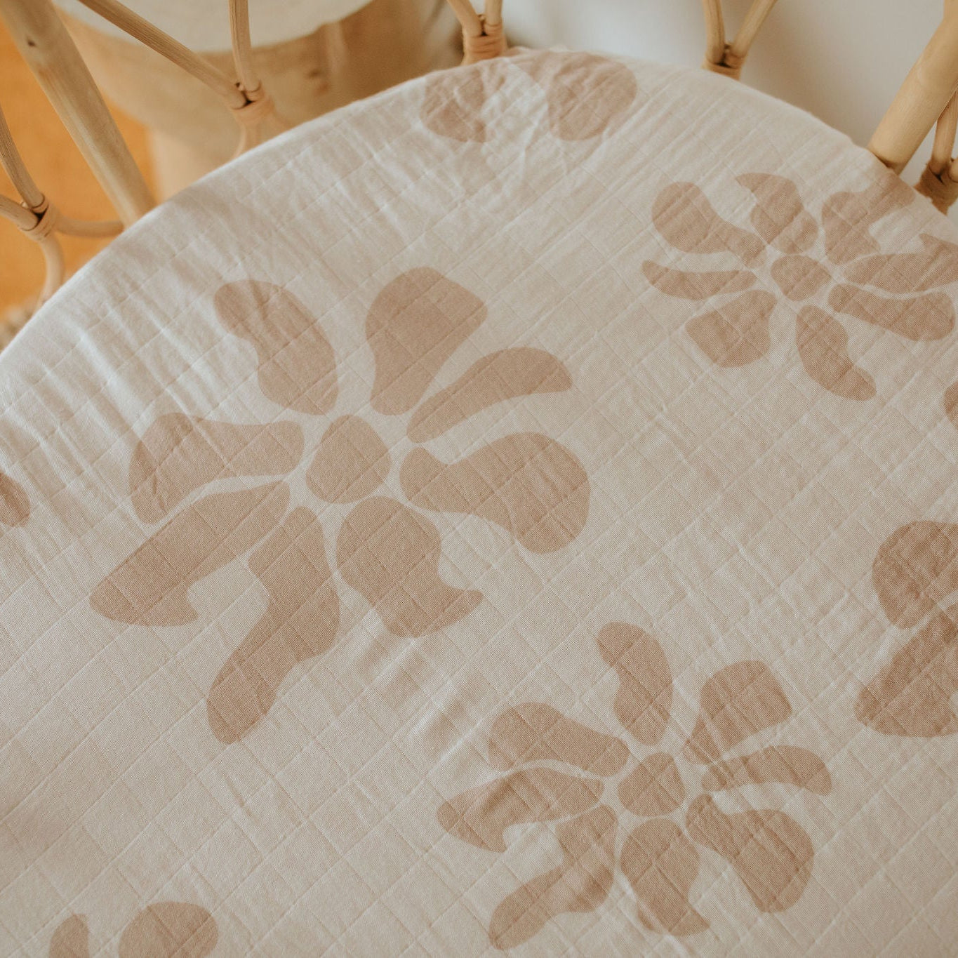 A fitted bassinet sheet with a floral print in blush pink colors, placed on a bassinet.