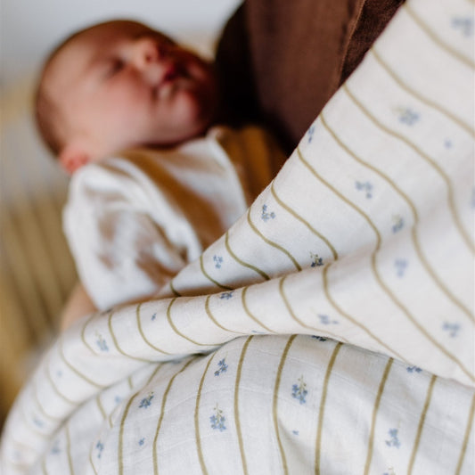 Newborn baby wrapped in a white blanket with blue floral patterns, lying on a brown surface.