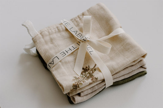 A stack of beige organic cotton muslin cloths with a brand label tied with a ribbon, designed in Wanaka, New Zealand.